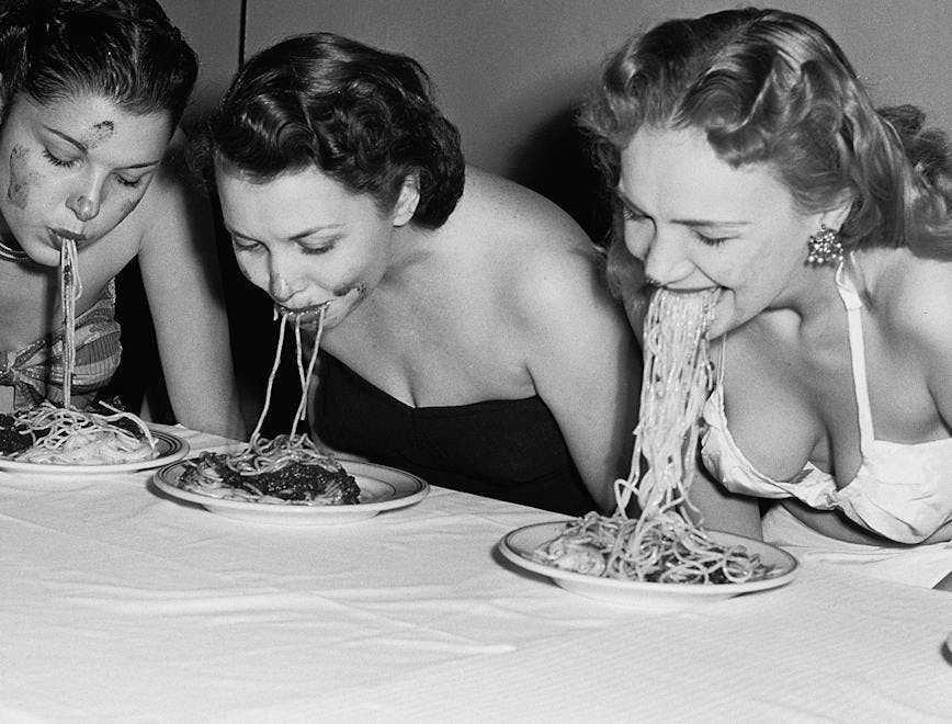 eating fun rivalry women head and shoulders portrait caucasian ethnicity dinner plate competitor flower arrangement spaghetti tablecloth american eating contest swimwear five people new york city table person human dish food meal