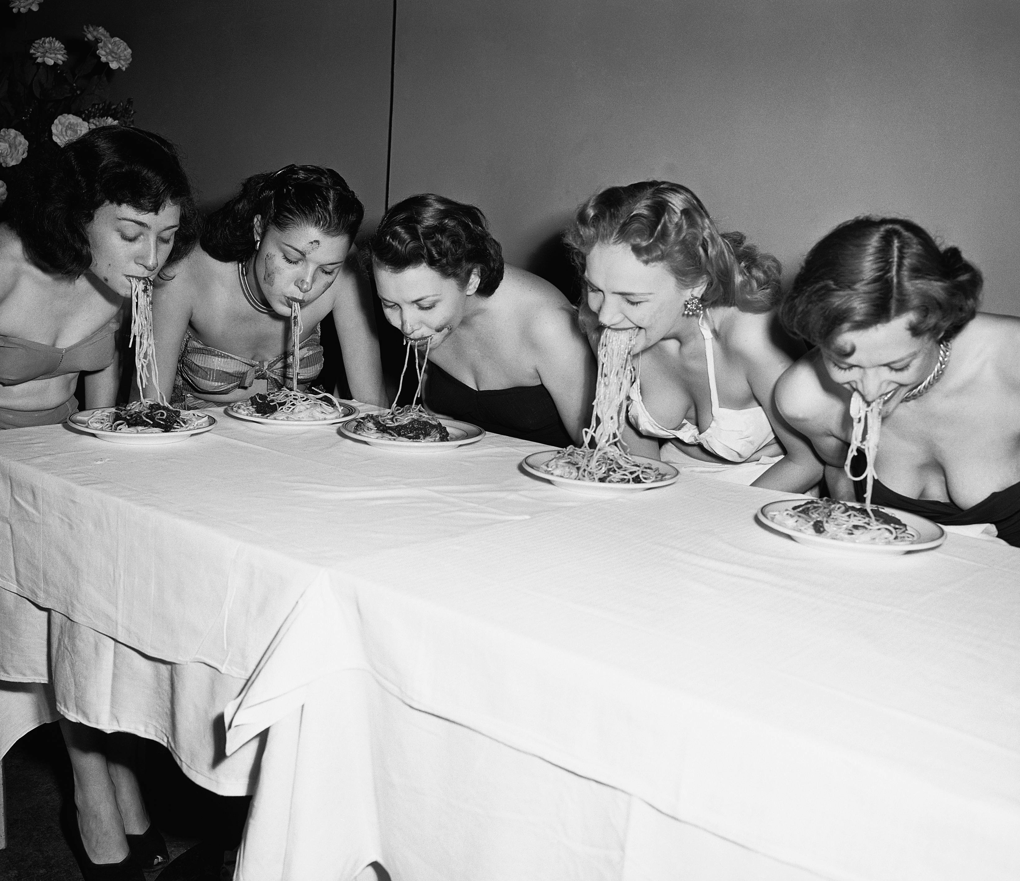 eating fun rivalry women head and shoulders portrait caucasian ethnicity dinner plate competitor flower arrangement spaghetti tablecloth american eating contest swimwear five people new york city table person human